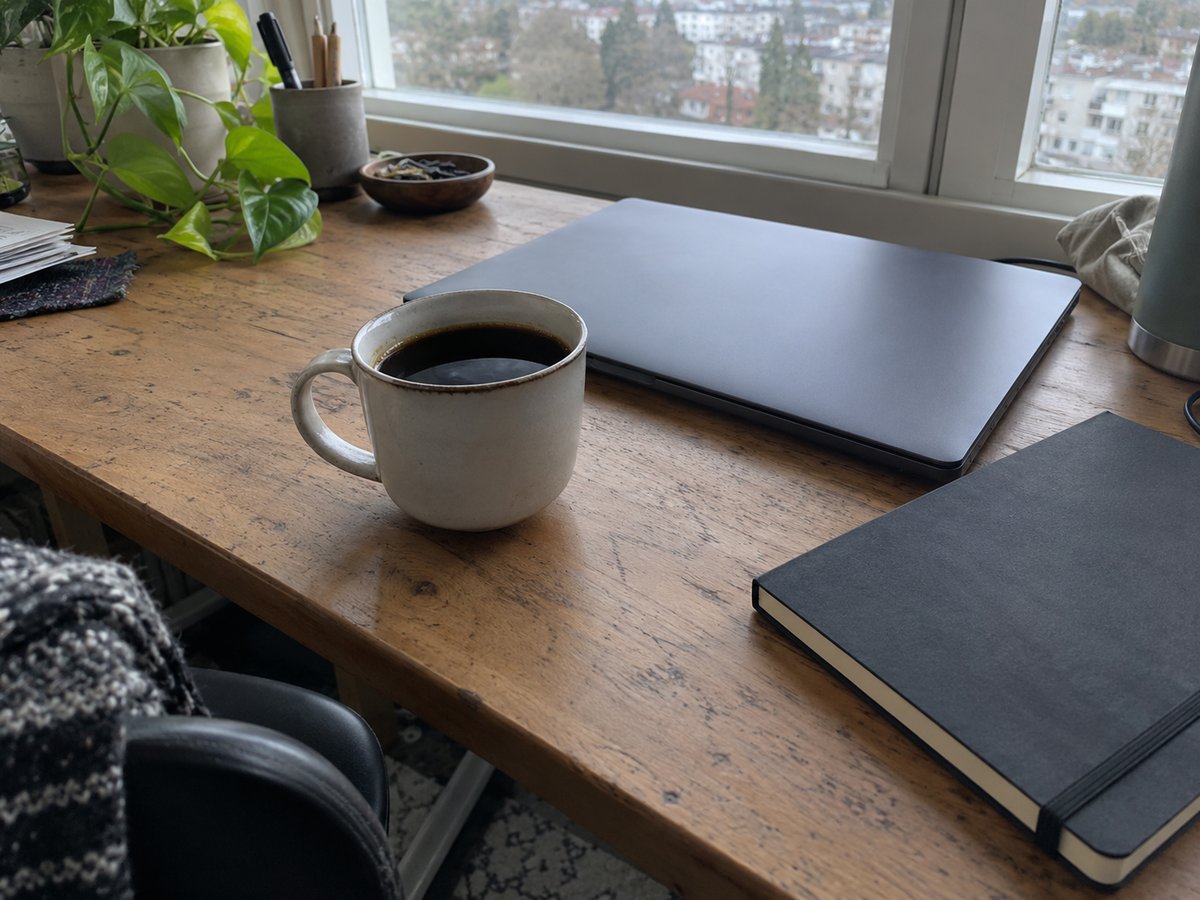Cup of black coffee on a wooden desk next to a closed laptop and a notebook