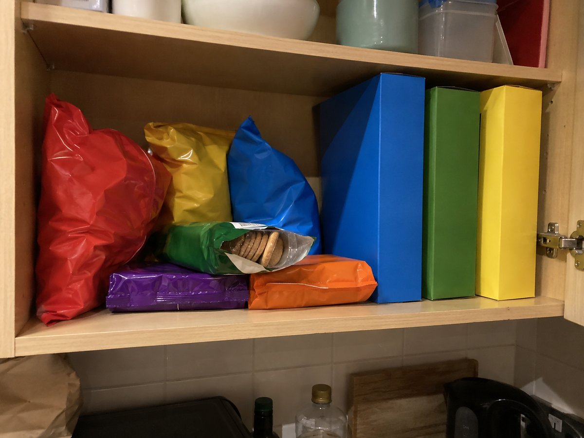 Open kitchen cupboard shelf with packets of crisps, biscuits and cereal boxes