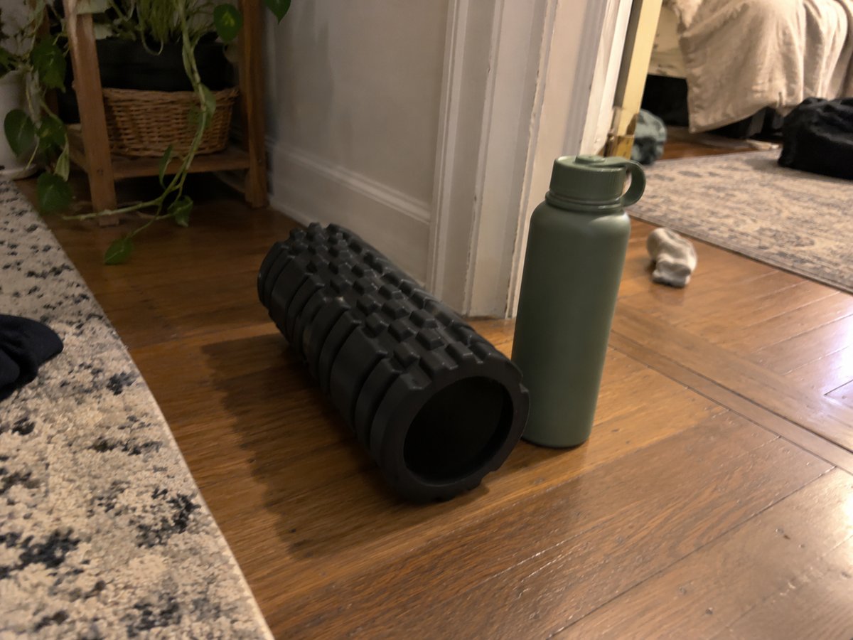 Black foam roller and a green reusable water bottle on a wooden floor