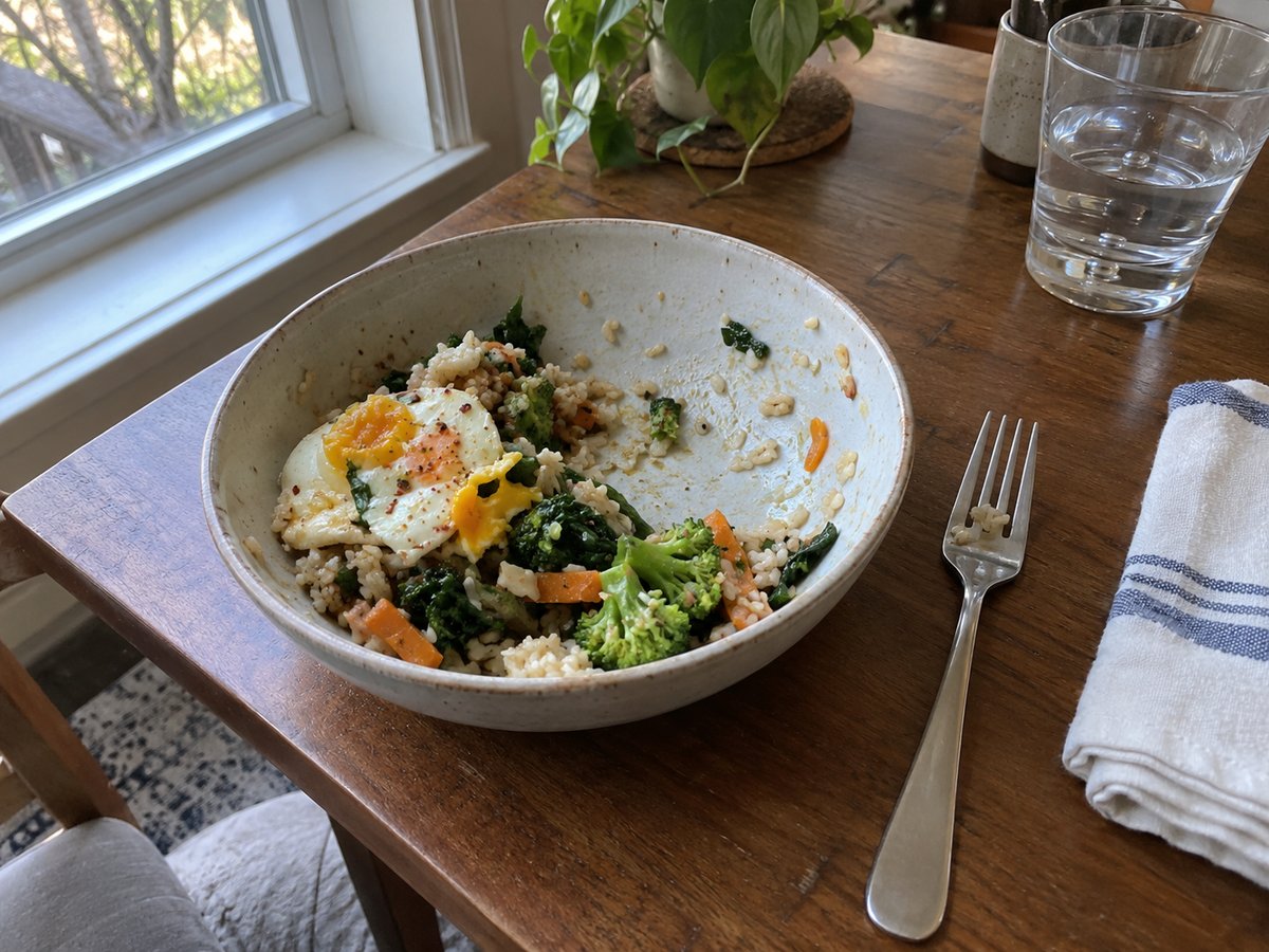 Half-eaten lunch bowl of rice, vegetables and egg on a table by the window