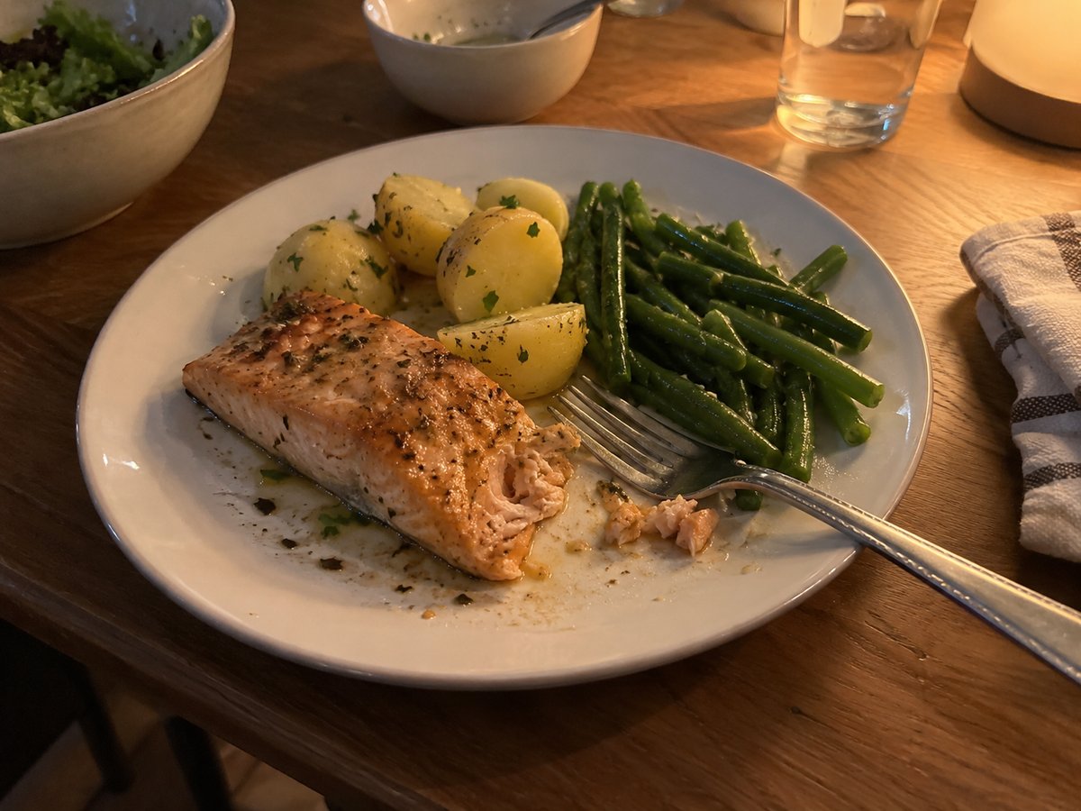Plate of baked salmon with boiled potatoes and green beans on a kitchen table