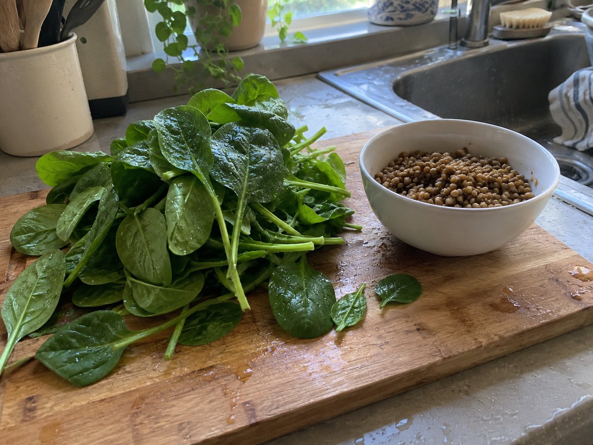 Bunch of fresh spinach and a bowl of cooked lentils on a cutting board by the sink